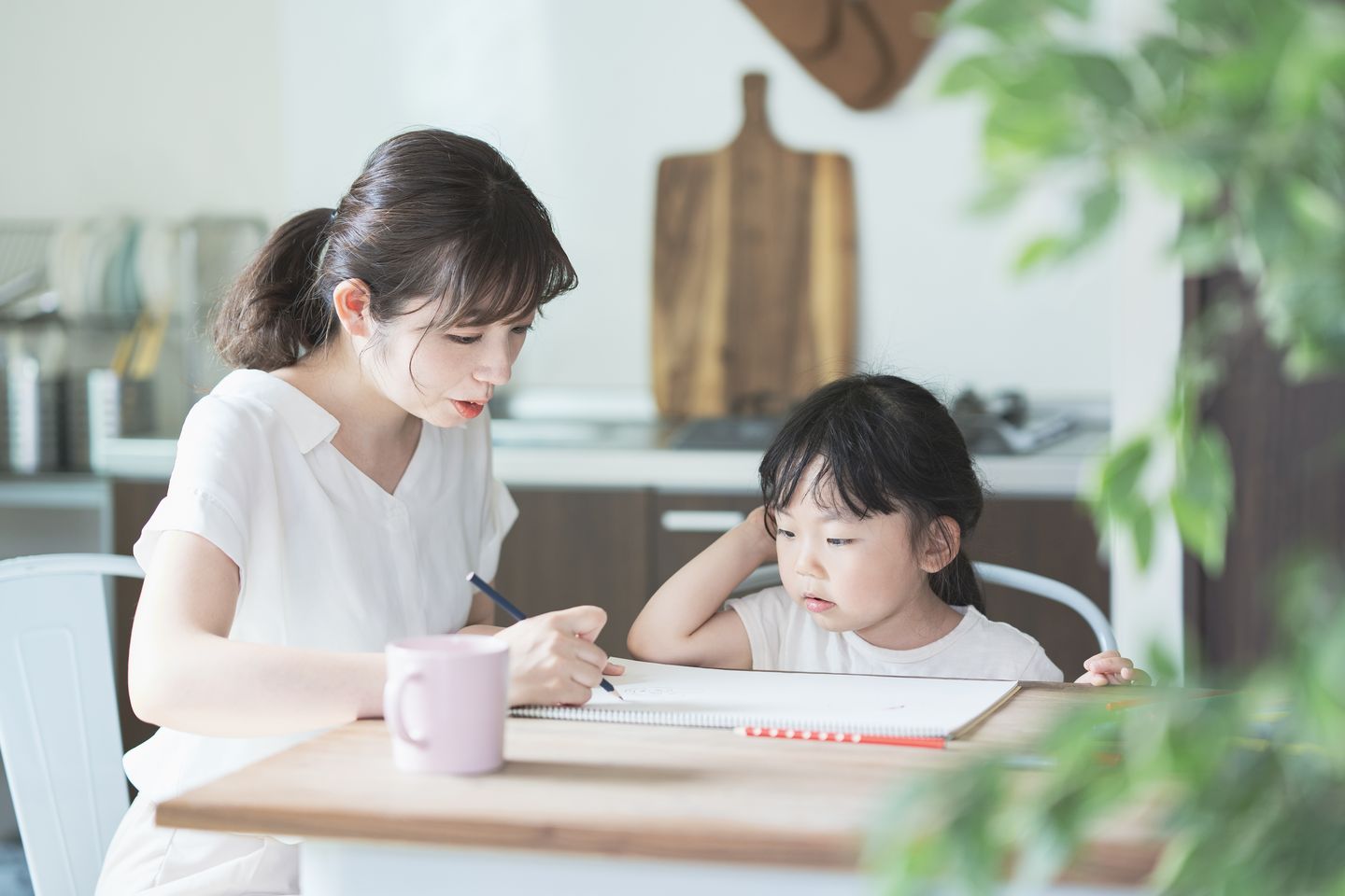 テーブルでお絵かきをする子どもと、隣で見守る母親